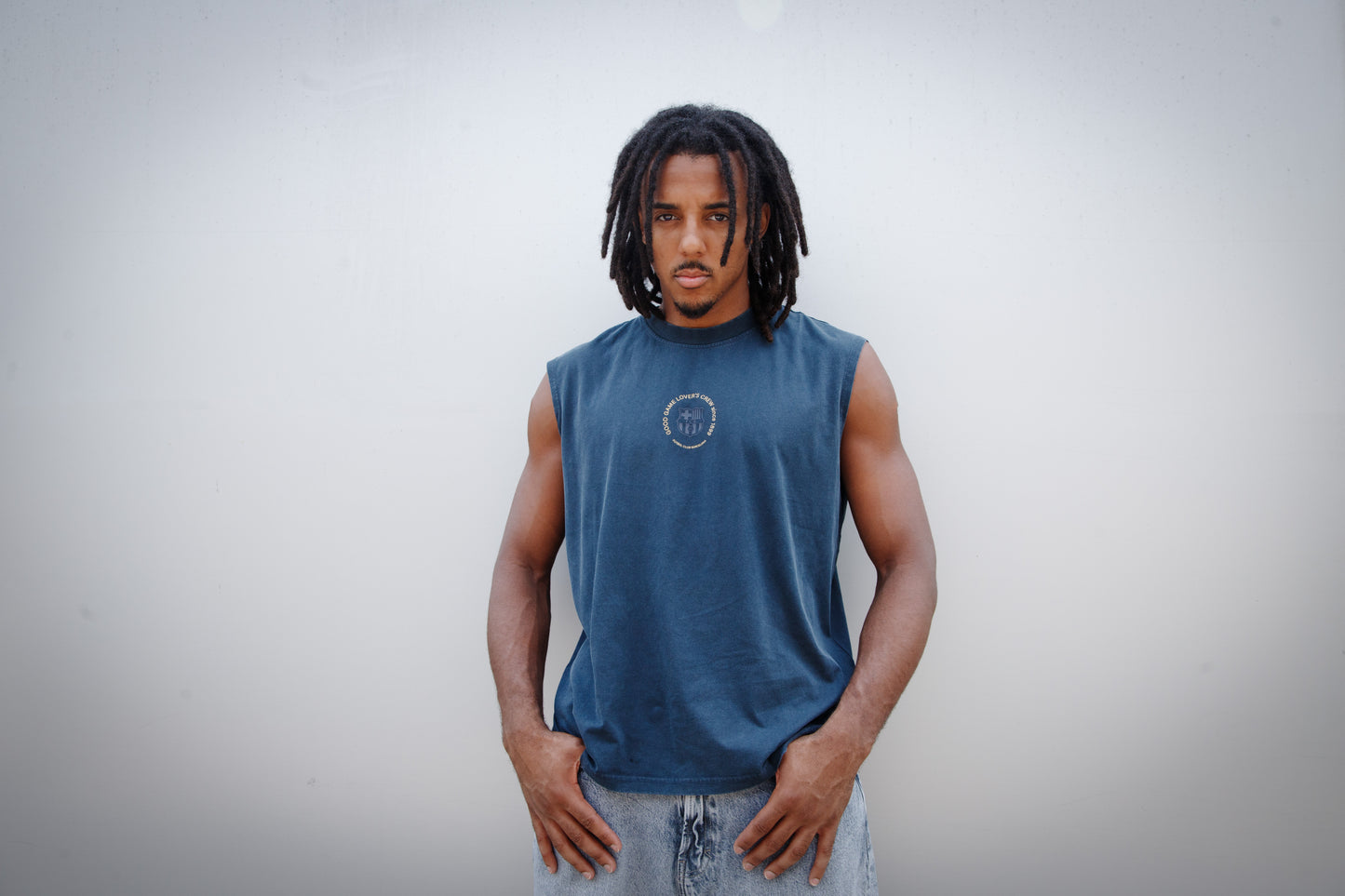 Jules Kounde wearing a sleeveless dark blue FC Barcelona T-shirt with circular crest print on the chest, paired with light denim jeans