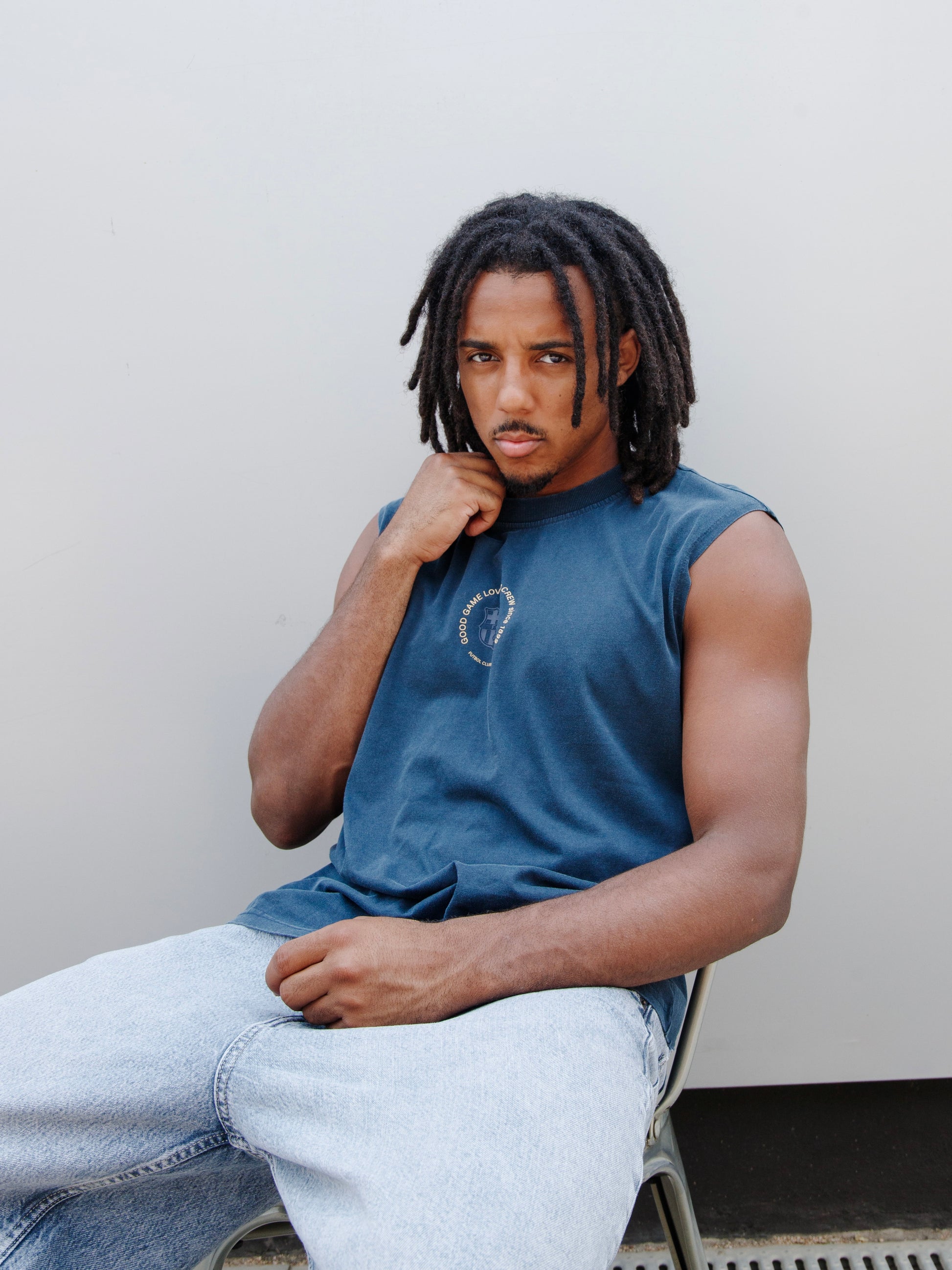 Jules Kounde wearing a sleeveless dark blue FC Barcelona T-shirt with circular crest print on the chest, paired with light denim jeans