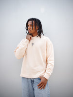 Jules Kounde wearing a light peach FC Barcelona sweatshirt with circular crest print on the chest, paired with light blue denim jeans.