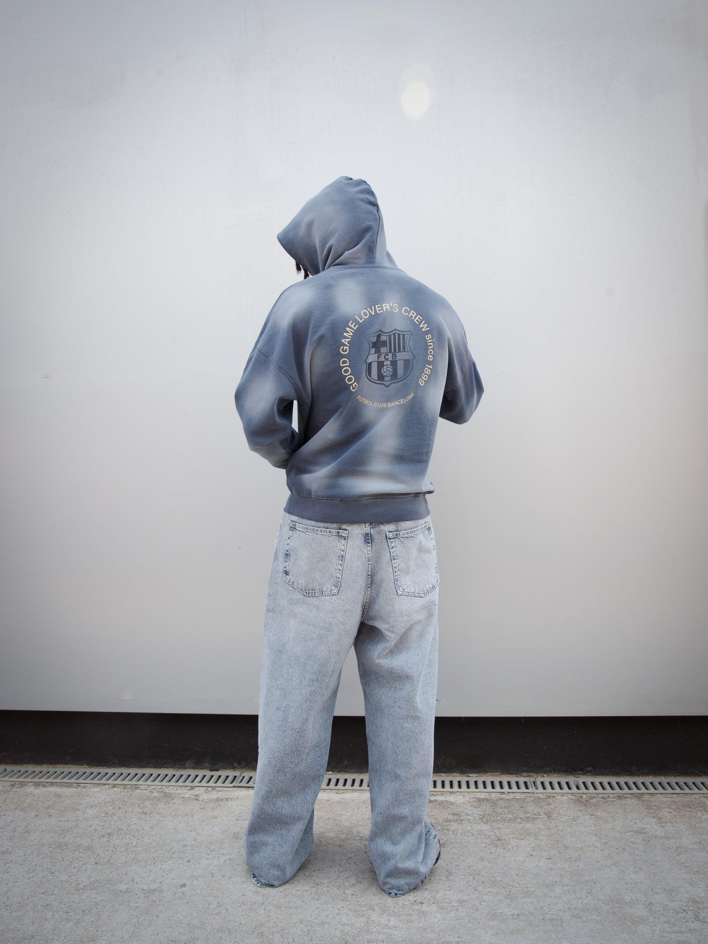 Jules Kounde wearing a faded blue FC Barcelona hoodie with kangaroo pocket and golden 'Barça' text design, paired with light denim jeans