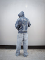 Jules Kounde wearing a faded blue FC Barcelona hoodie with kangaroo pocket and golden 'Barça' text design, paired with light denim jeans