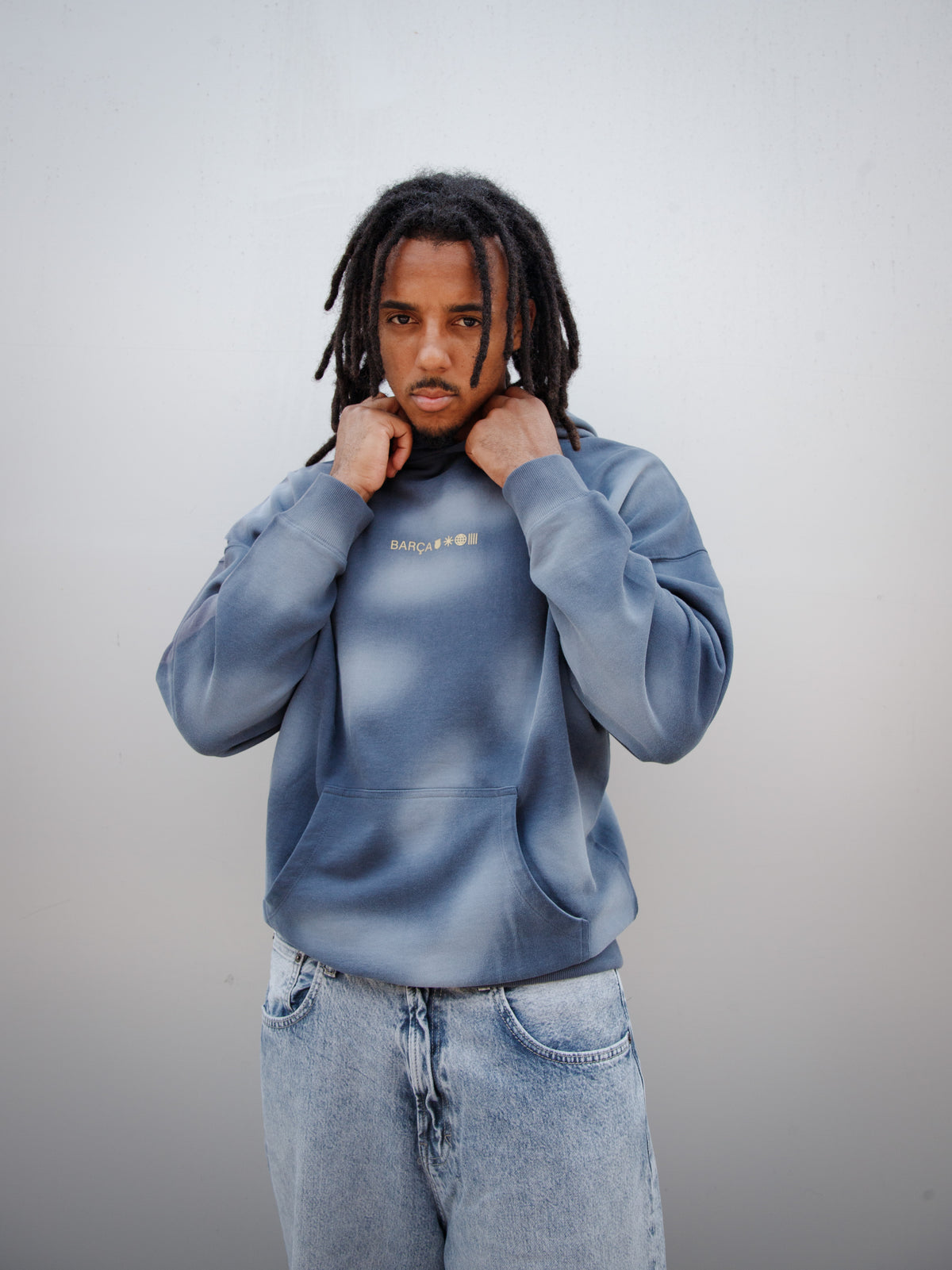 Jules Kounde wearing a faded blue FC Barcelona hoodie with kangaroo pocket and golden 'Barça' text design, paired with light denim jeans