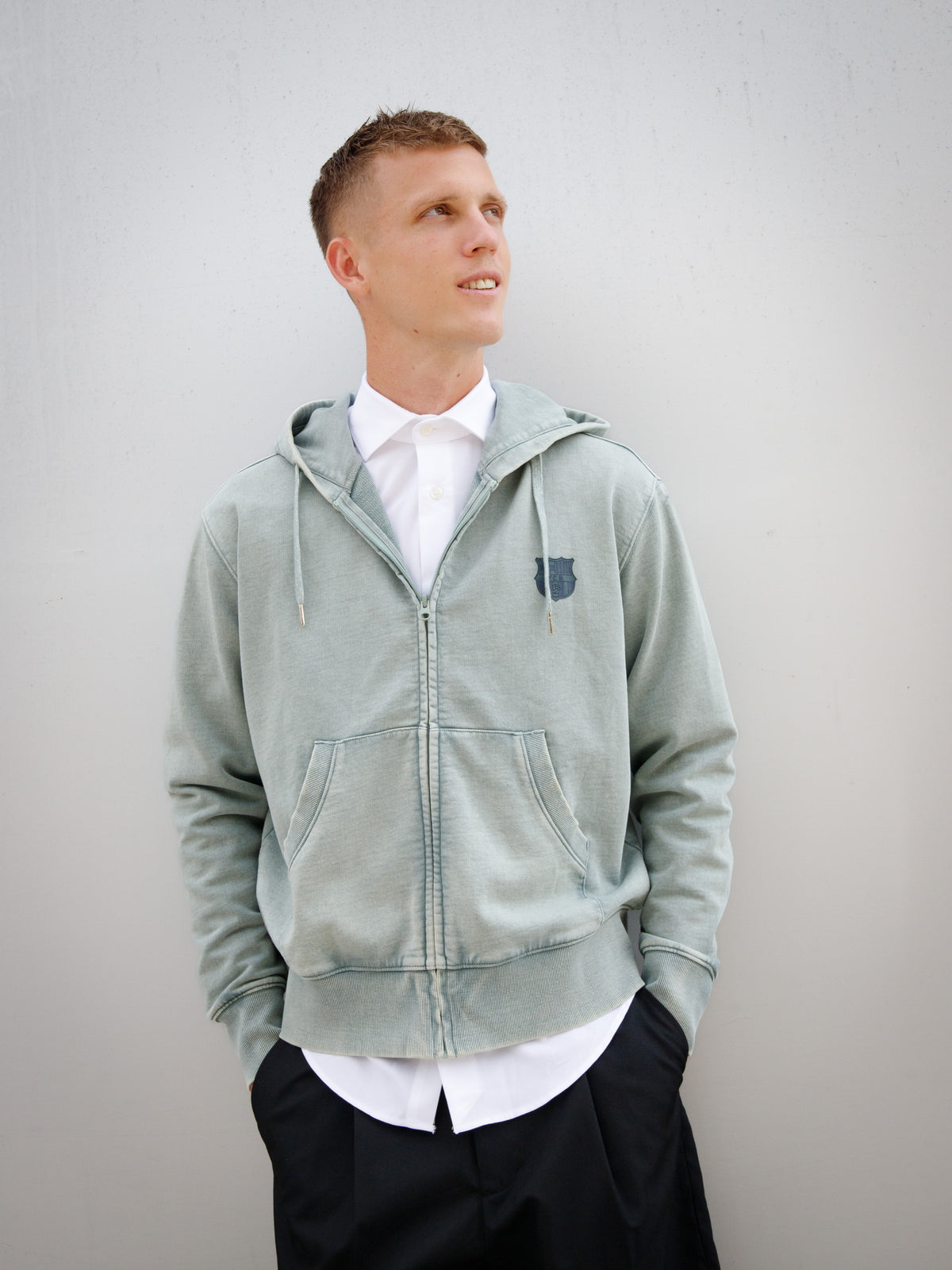 Dani Olmo wearing a light green FC Barcelona zip-up hoodie with tonal crest, paired with a white shirt and black shorts.