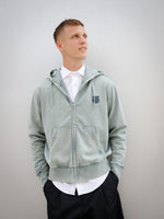 Dani Olmo wearing a light green FC Barcelona zip-up hoodie with tonal crest, paired with a white shirt and black shorts.