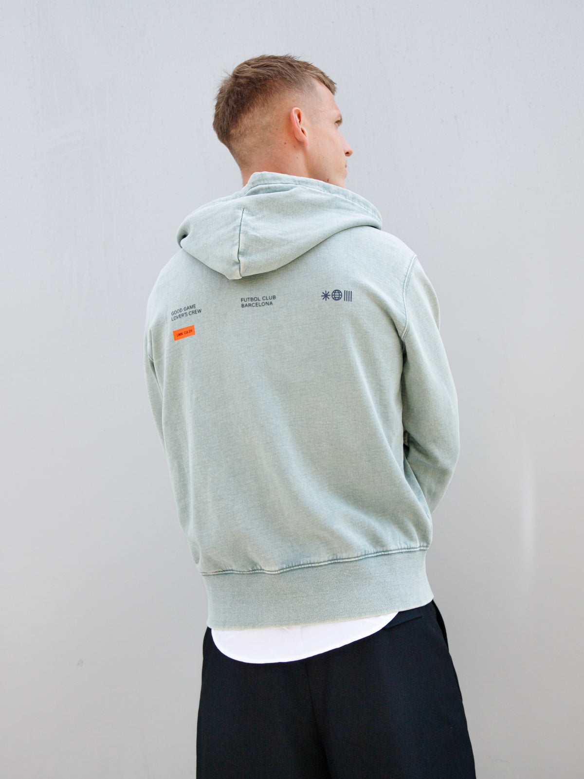 Dani Olmo wearing a light green FC Barcelona zip-up hoodie with tonal crest, paired with a white shirt and black shorts.