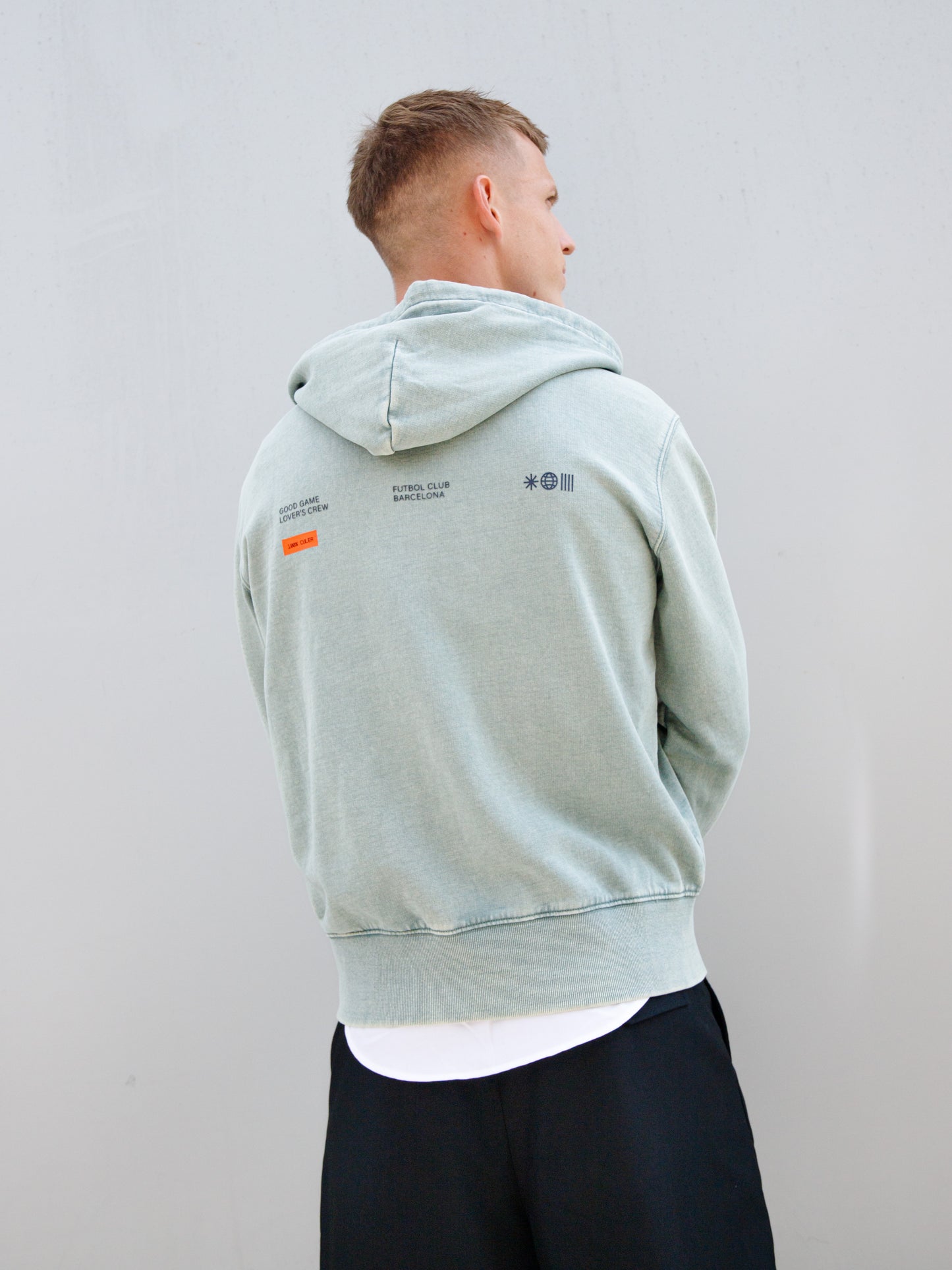 Dani Olmo wearing a light green FC Barcelona zip-up hoodie with tonal crest, paired with a white shirt and black shorts.