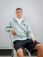 Dani Olmo wearing a light green FC Barcelona zip-up hoodie with tonal crest, paired with a white shirt and black shorts.