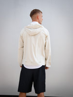 Dani Olmo wearing a light beige FC Barcelona hooded jacket with subtle crest and orange detail, paired with black shorts and white polo shirt