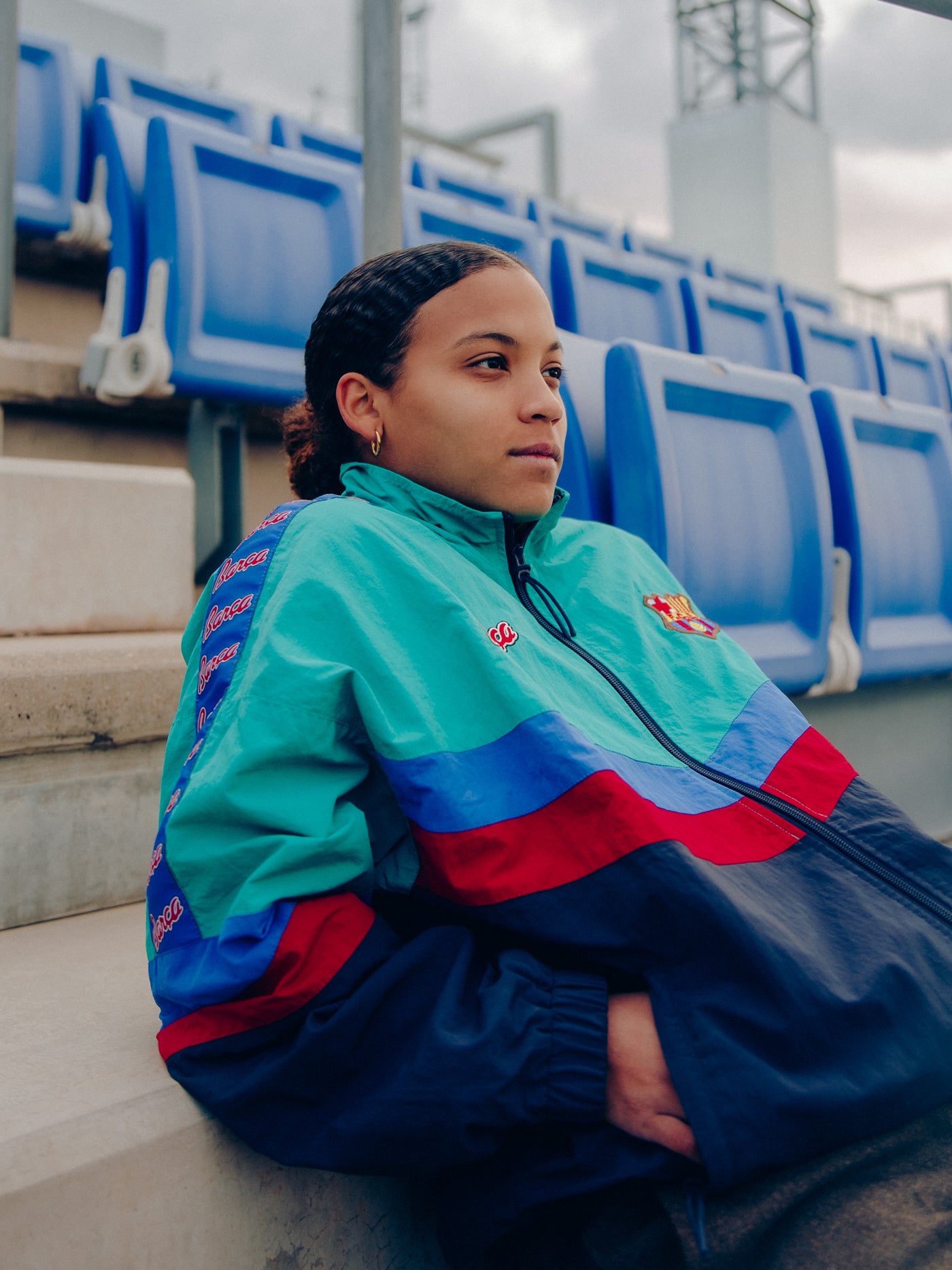 Retro-style windbreaker in teal, red, blue, and navy with FC Barcelona crest and embroidered 'Barça' text on the chest.