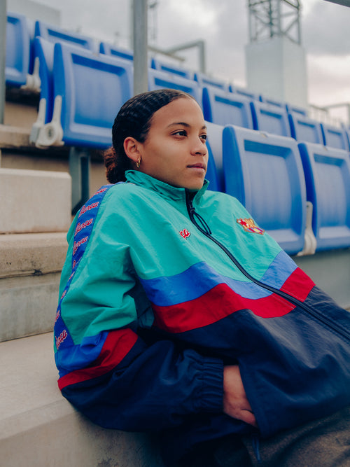 Retro-style windbreaker in teal, red, blue, and navy with FC Barcelona crest and embroidered 'Barça' text on the chest.