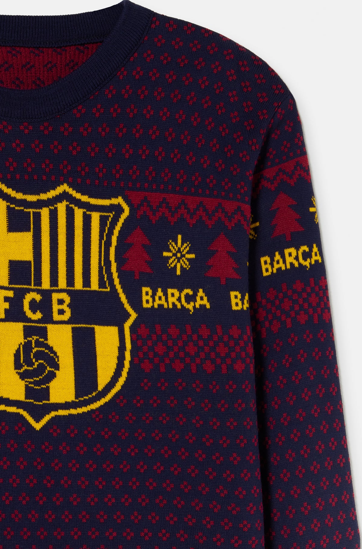 Primer plano de un jersey azul marino de FC Barcelona con un gran escudo amarillo y un motivo de punto festivo rojo en el pecho y la manga.