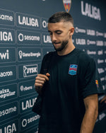 Modèle portant un maillot noir du Barça avec l’écusson BARÇA sur la poitrine et le patch de LaLiga sur la manche, devant un fond de sponsors de LaLiga.