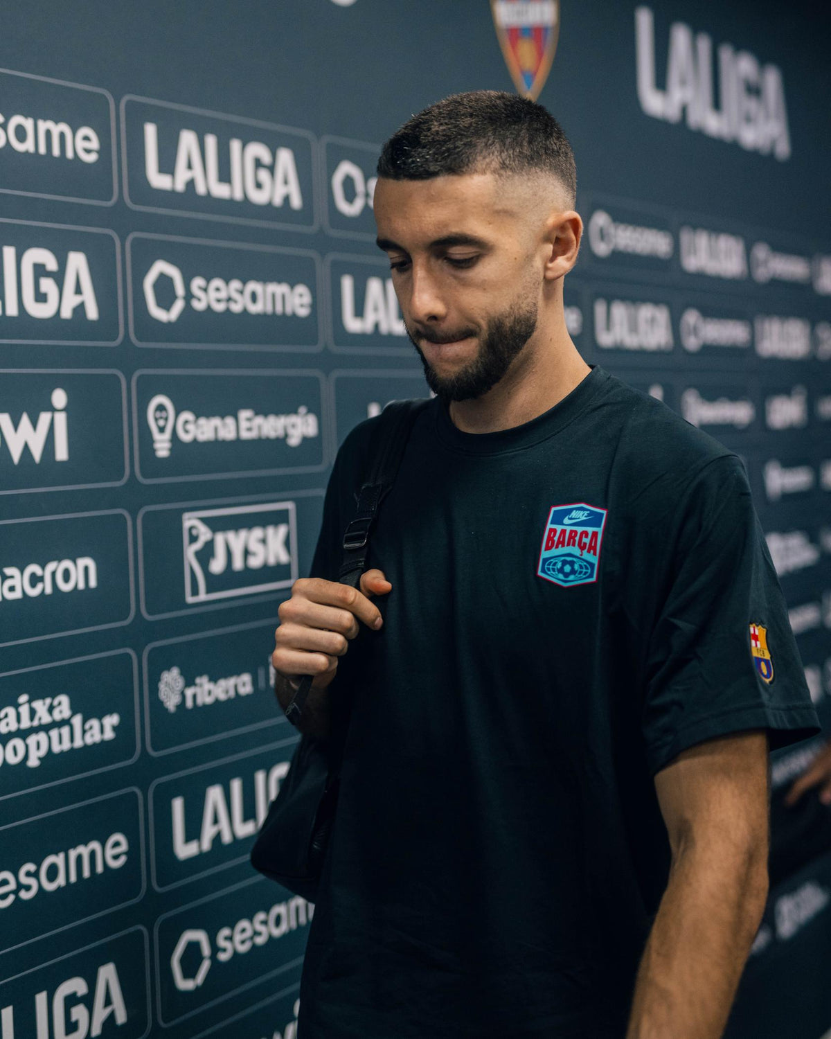 Modèle portant un maillot noir du Barça avec l’écusson BARÇA sur la poitrine et le patch de LaLiga sur la manche, devant un fond de sponsors de LaLiga.
