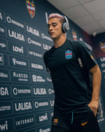 Footballeur portant un haut d'entraînement noir FC Barcelona et un short avec casque dans un tunnel de stade.