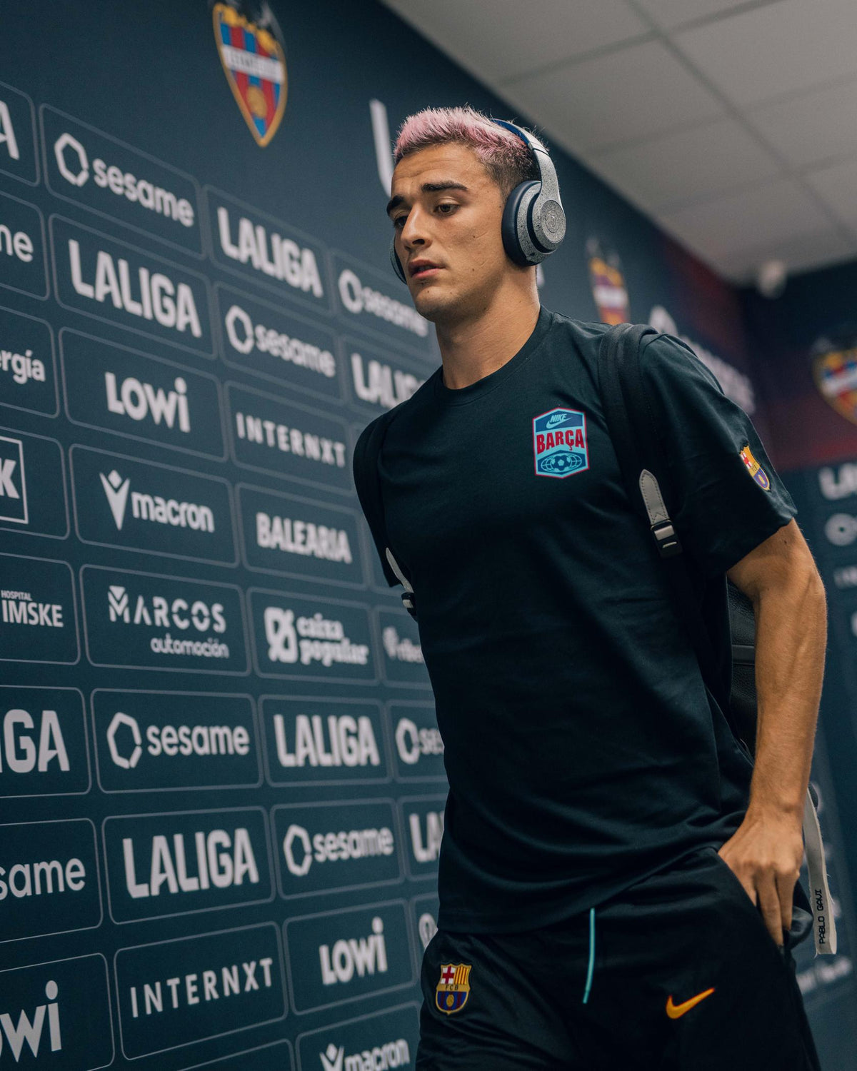 Footballeur portant un haut d'entraînement noir FC Barcelona et un short avec casque dans un tunnel de stade.