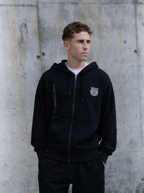 Model wearing a black FC Barcelona zip hoodie with tonal crest detail.