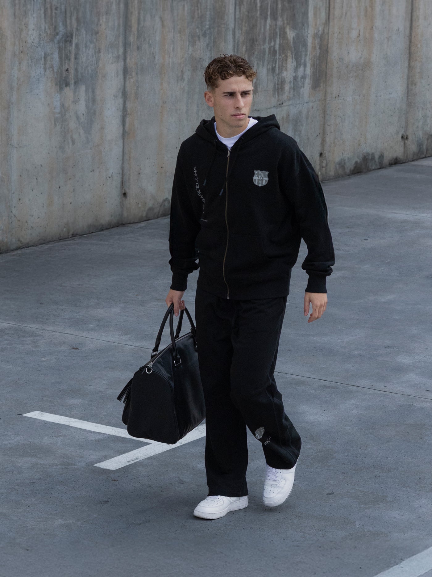 Man in black hoodie and pants holding a black bag in an urban setting