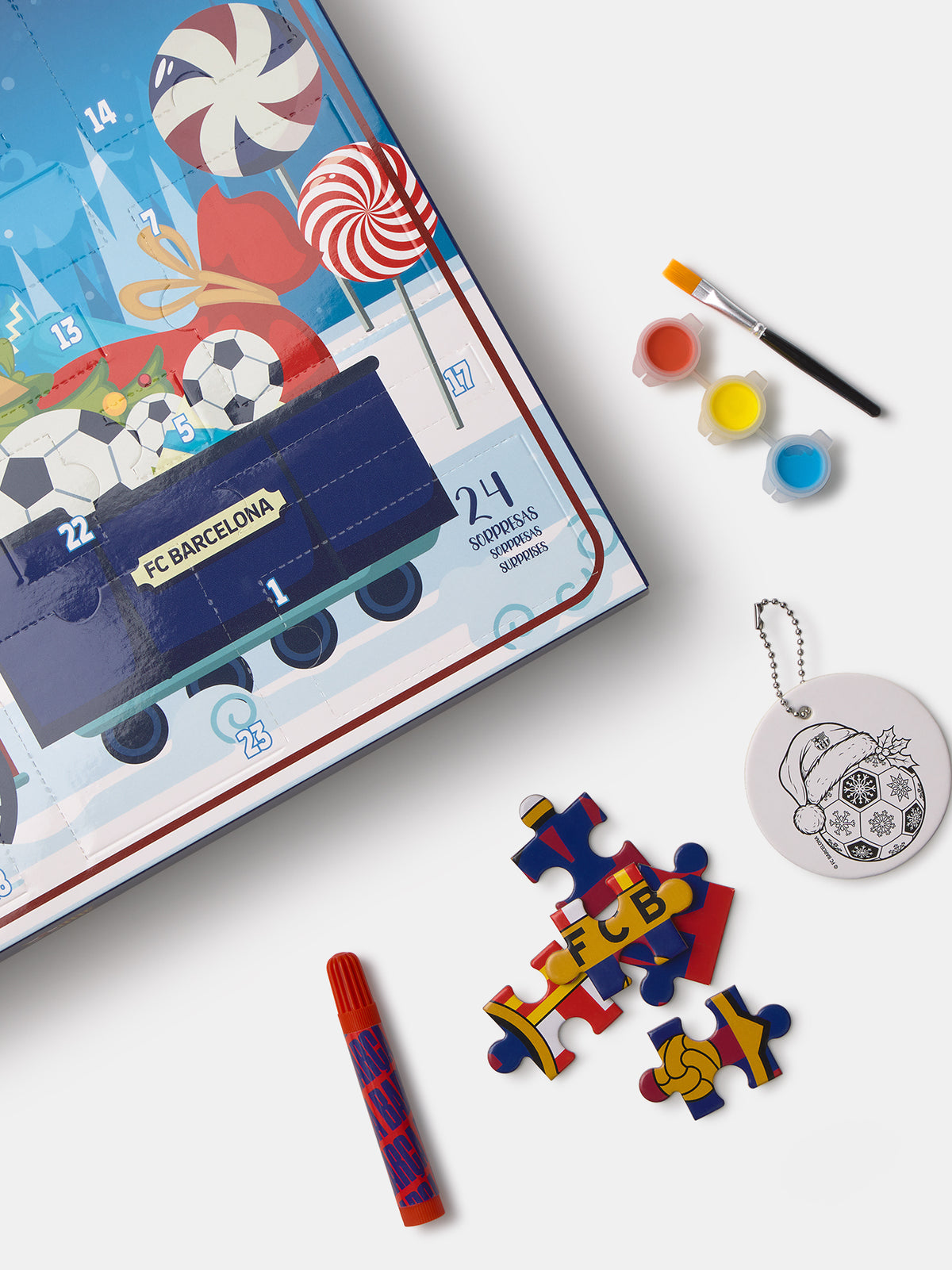 Boîte calendrier de l’Avent FC Barcelona avec bonbons et graphiques de football, montrée avec un pinceau, des pots de peinture, des pièces de puzzle et un ornement rond pour porte-clés.