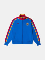 Vue de face d’une veste zippée bleue FC Barcelona avec manches bordeaux, bandes latérales jaunes, logo Nike et écusson du club.