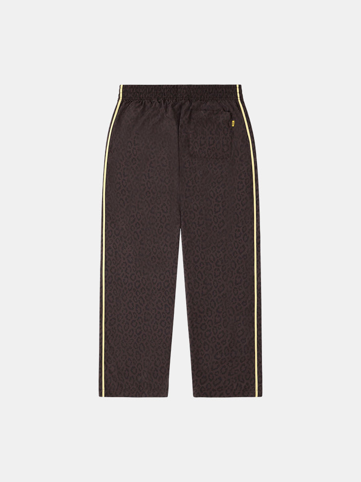 Vista frontal de un pantalón de chándal marrón oscuro de FC Barcelona con estampado de leopardo, franjas laterales amarillas y cintura elástica.