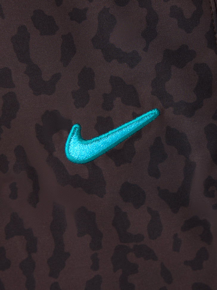 Primer plano del swoosh Nike turquesa bordado sobre tejido de camuflaje marrón oscuro y negro.