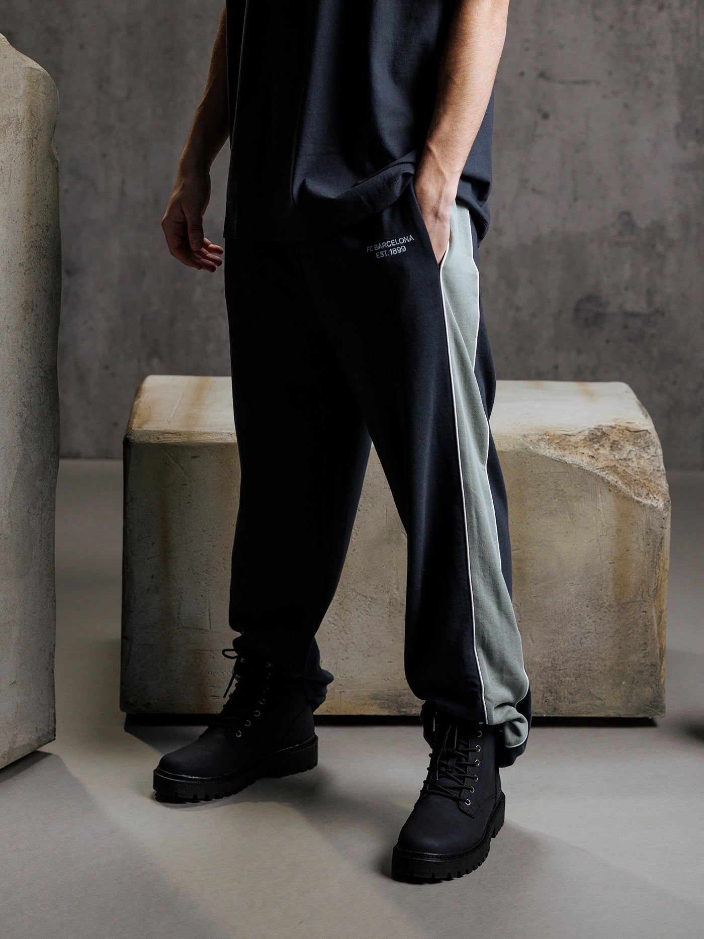 Person wearing black and gray pants with black boots in a minimalistic setting.