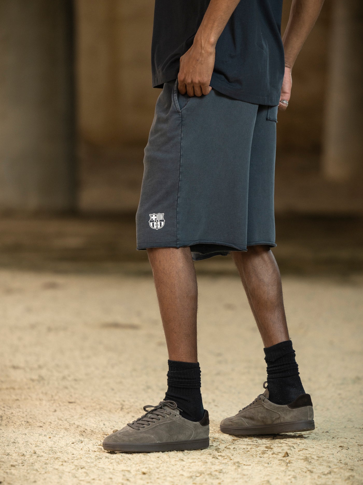 Person wearing dark shorts with a logo, black socks, and gray shoes on a blurred background