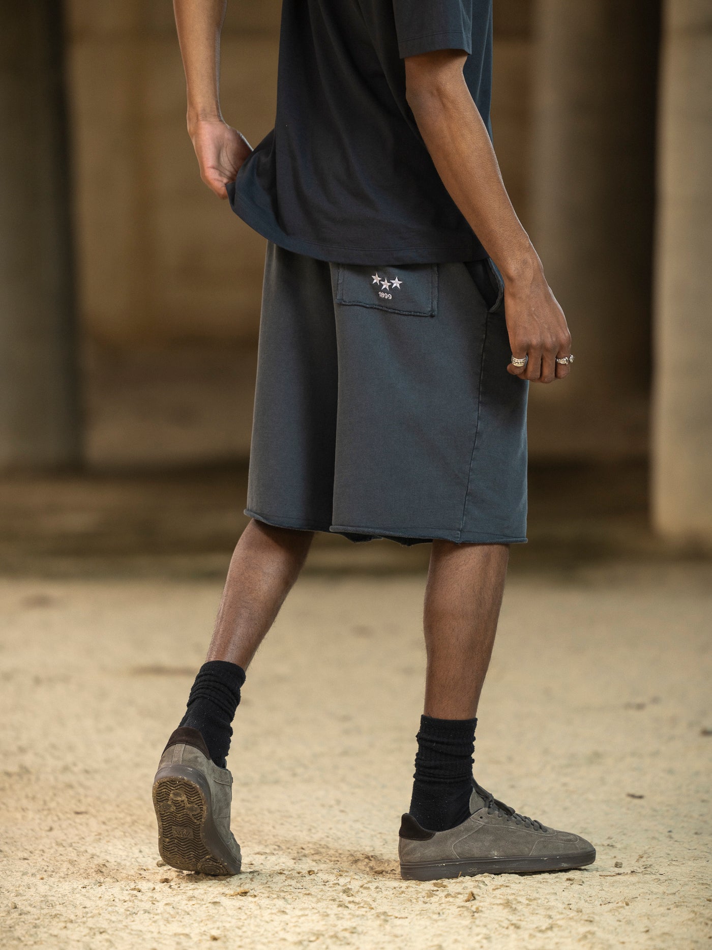 Person wearing a dark shirt, gray shorts, and black socks with shoes on a blurred background