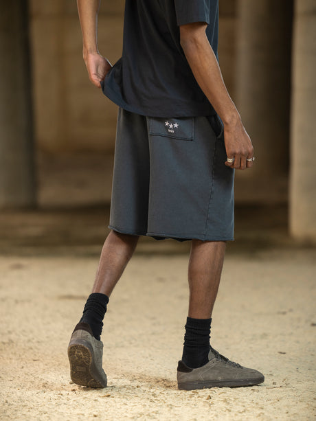 Person wearing a dark shirt, gray shorts, and black socks with shoes on a blurred background