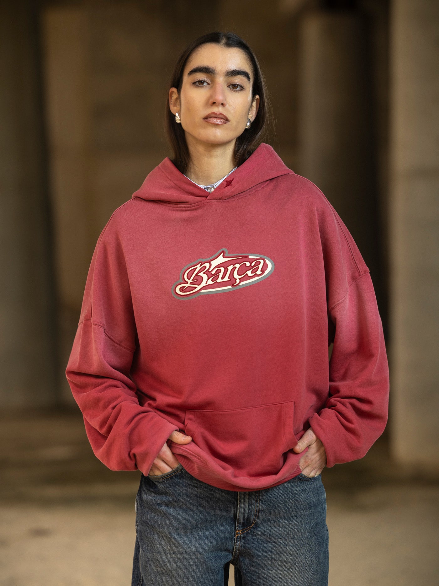 Person wearing a red hoodie with a logo, standing against a blurred background