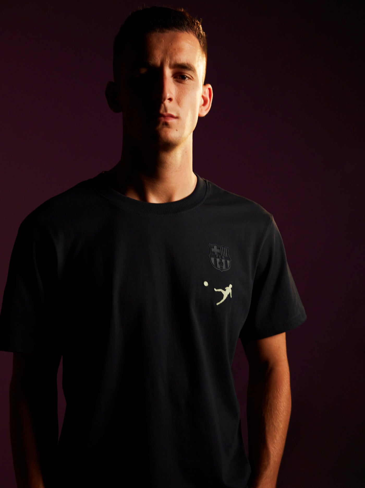 Person wearing a black T-shirt featuring 'Barça X Johan Cruyff' and the number 9 printed on the back, in a dimly lit setting with a purple background.