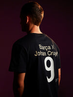 Person wearing a black T-shirt featuring 'Barça X Johan Cruyff' and the number 9 printed on the back, in a dimly lit setting with a purple background.