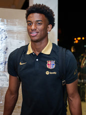 Model wearing a navy FC Barcelona polo shirt with a gold collar, Nike swoosh and Spotify logo, shown frontally with backpack straps.