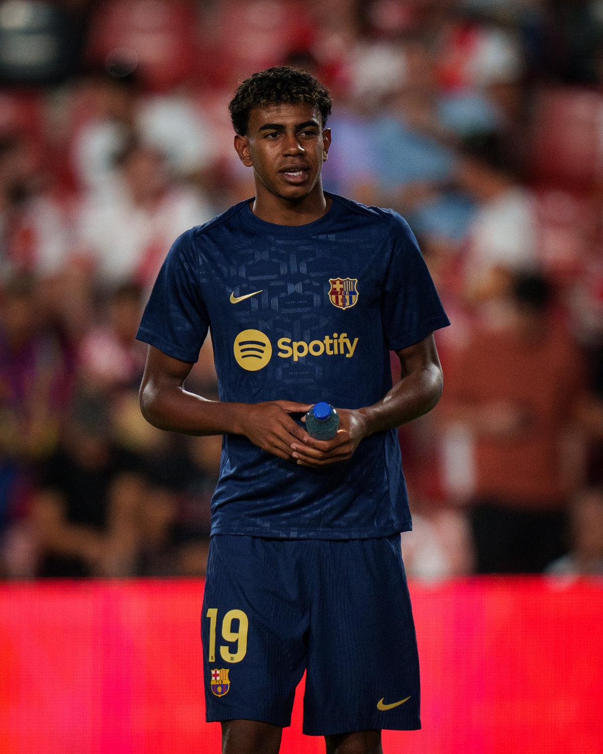 FC Barcelona training shirt in dark navy blue featuring subtle tonal geometric patterns. The shirt displays a golden Nike swoosh on the right chest, the FC Barcelona crest on the left chest, and a bold gold Spotify logo centered across the front.