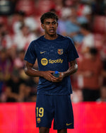 FC Barcelona training shirt in dark navy blue featuring subtle tonal geometric patterns. The shirt displays a golden Nike swoosh on the right chest, the FC Barcelona crest on the left chest, and a bold gold Spotify logo centered across the front.