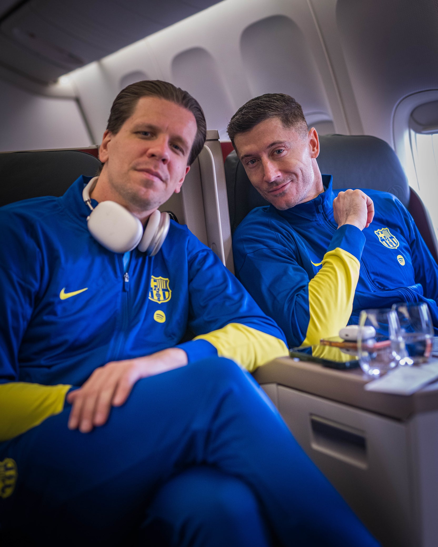 Two men in blue sports jackets sitting on an airplane.