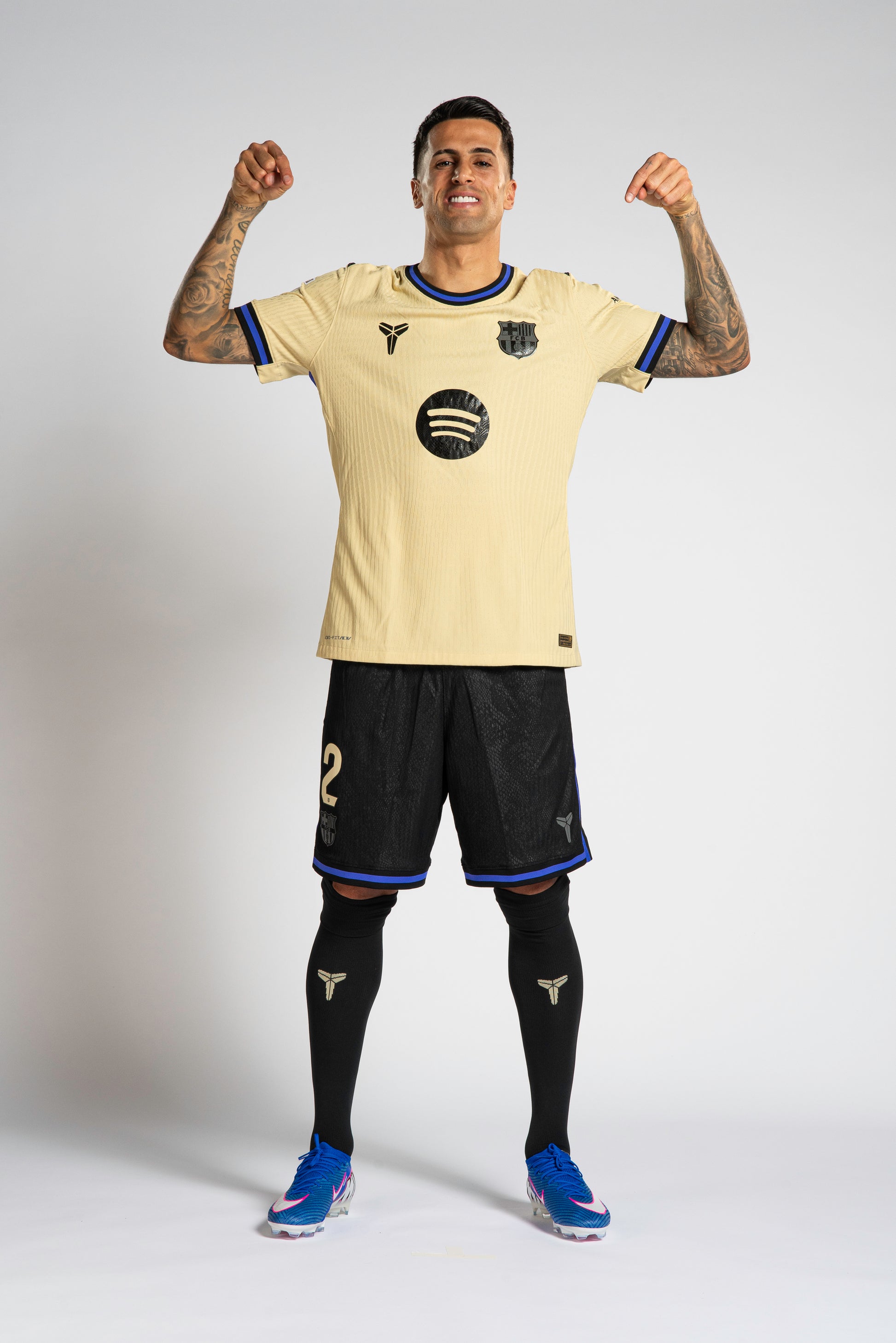 Cancelo wearing the Away Kit of FC Barcelona, a light yellow sports jersey with black shorts on a plain background