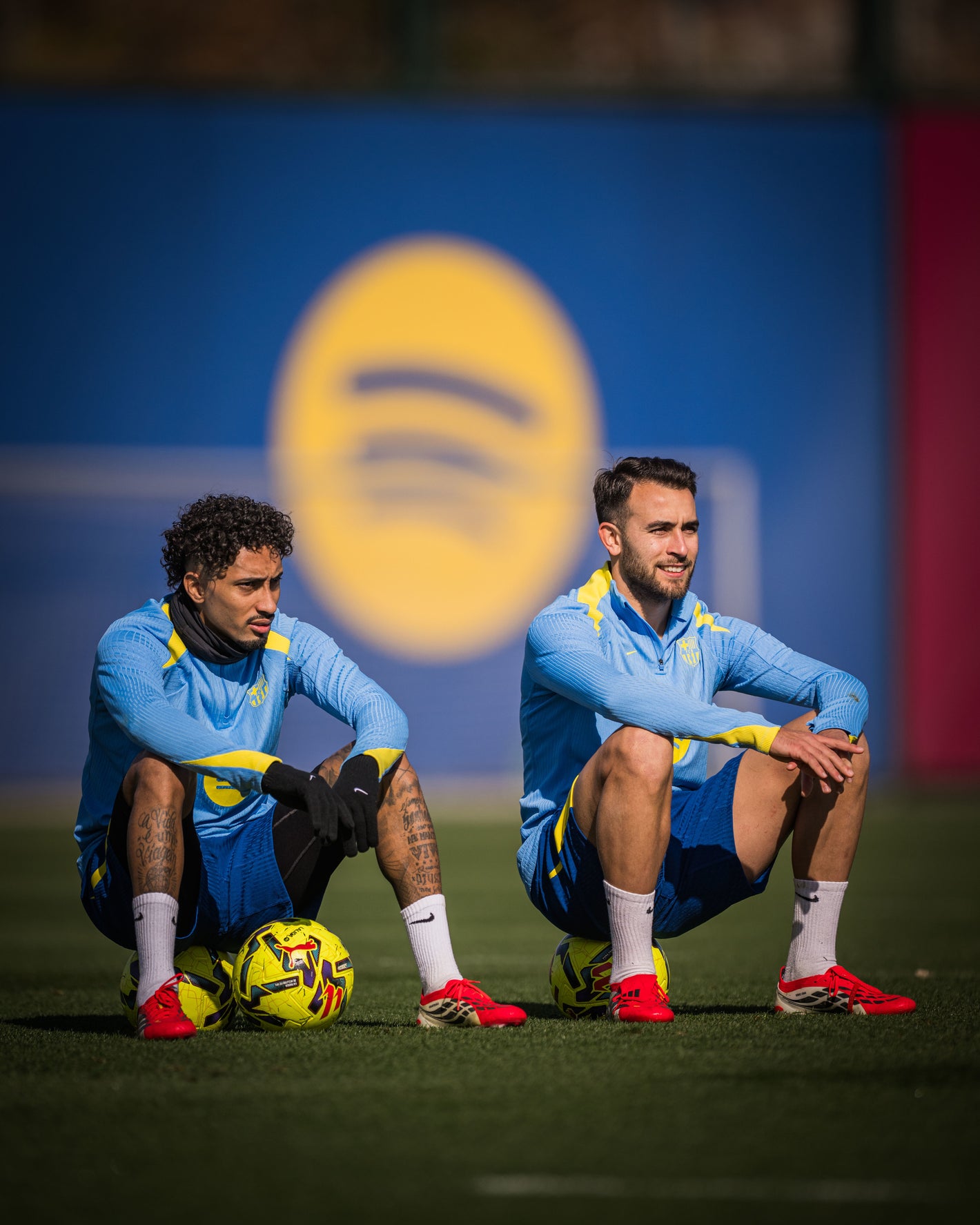 Raphinha and Eric in blue jerseys sitting on a field with a Spotify logo in the background.