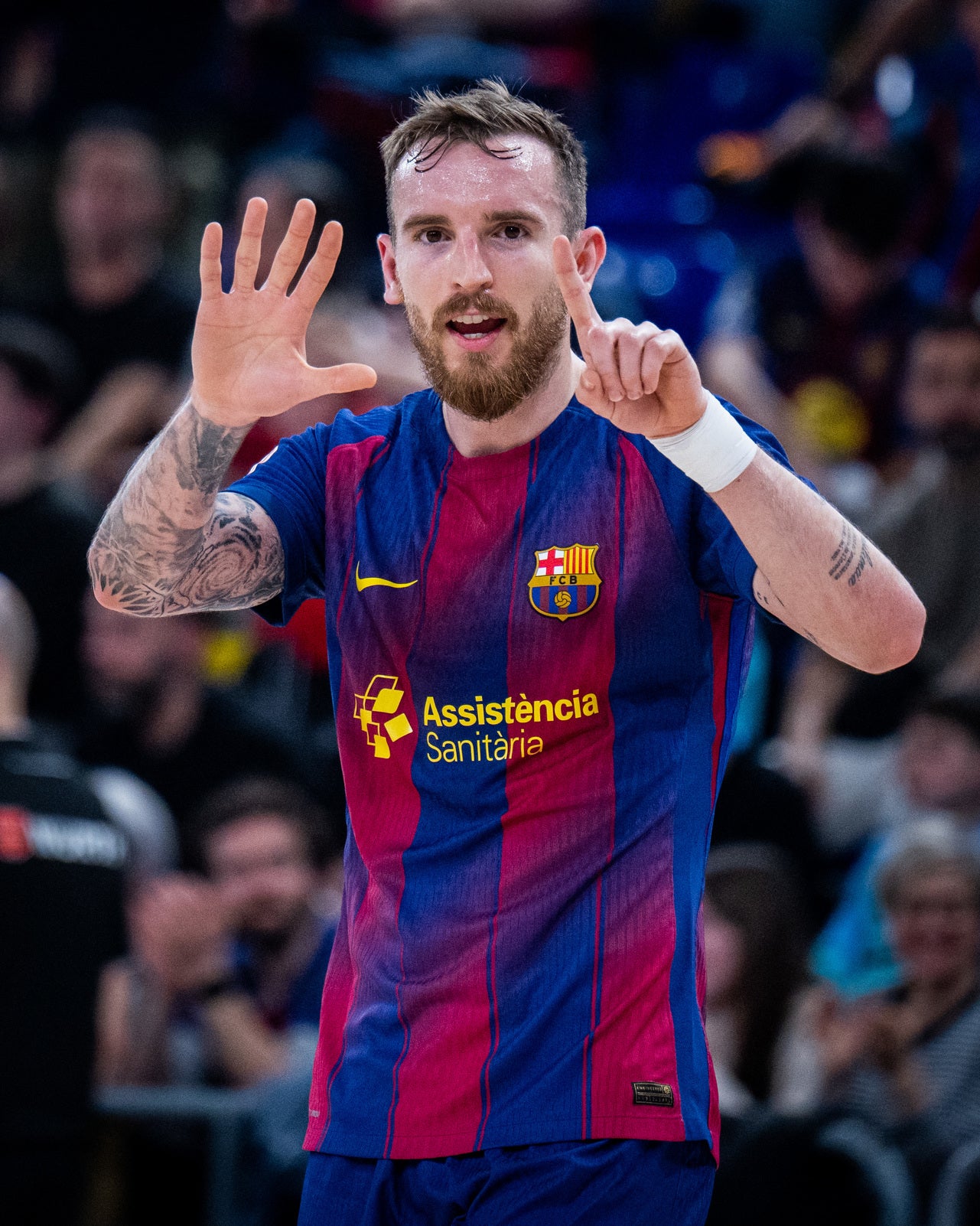 Person wearing a Barcelona soccer jersey with visible tattoos and a beard, in front of a blurred crowd.