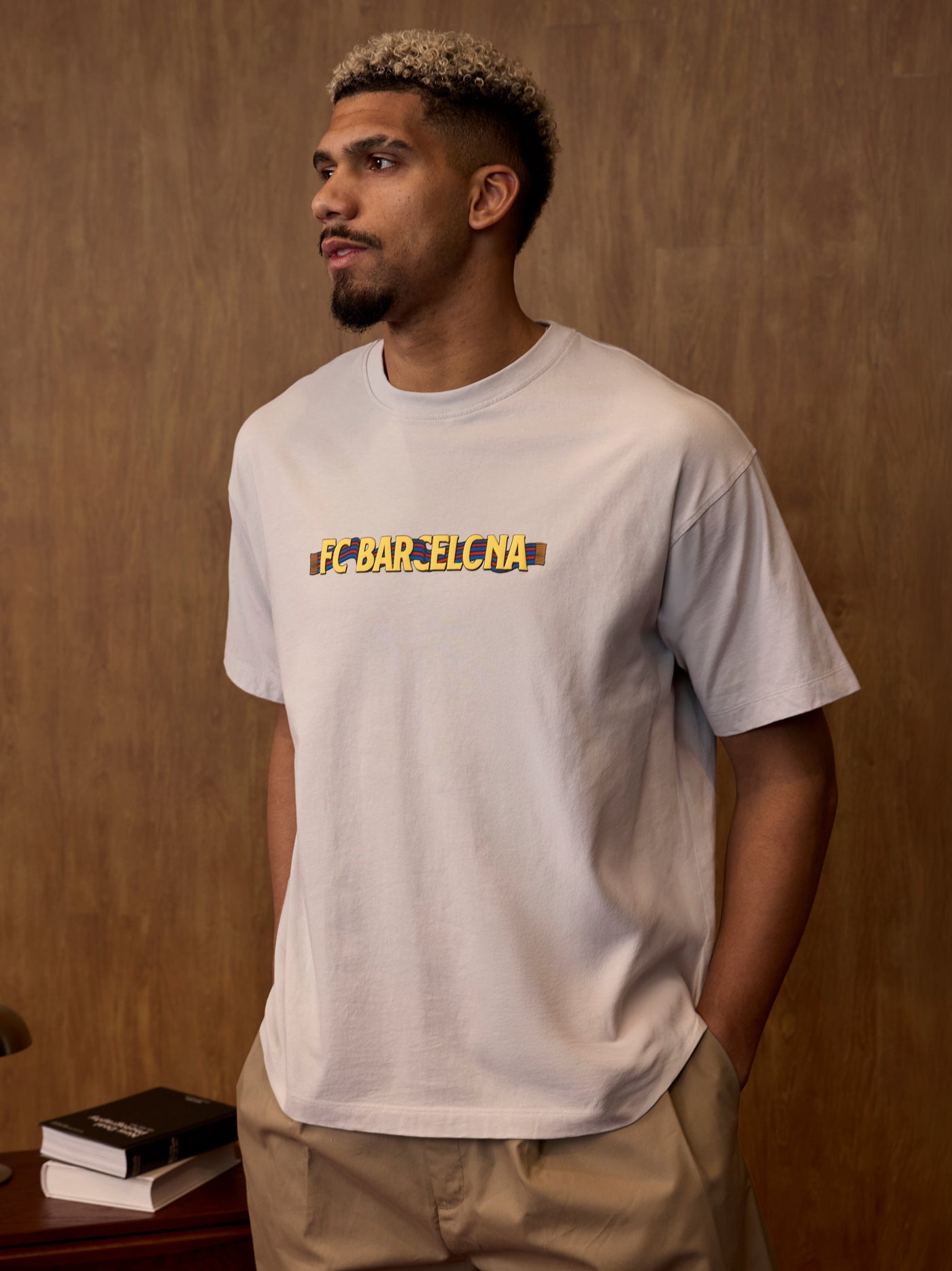 Man wearing a white t-shirt with 'FC BARCELONA' printed on it against a brown background