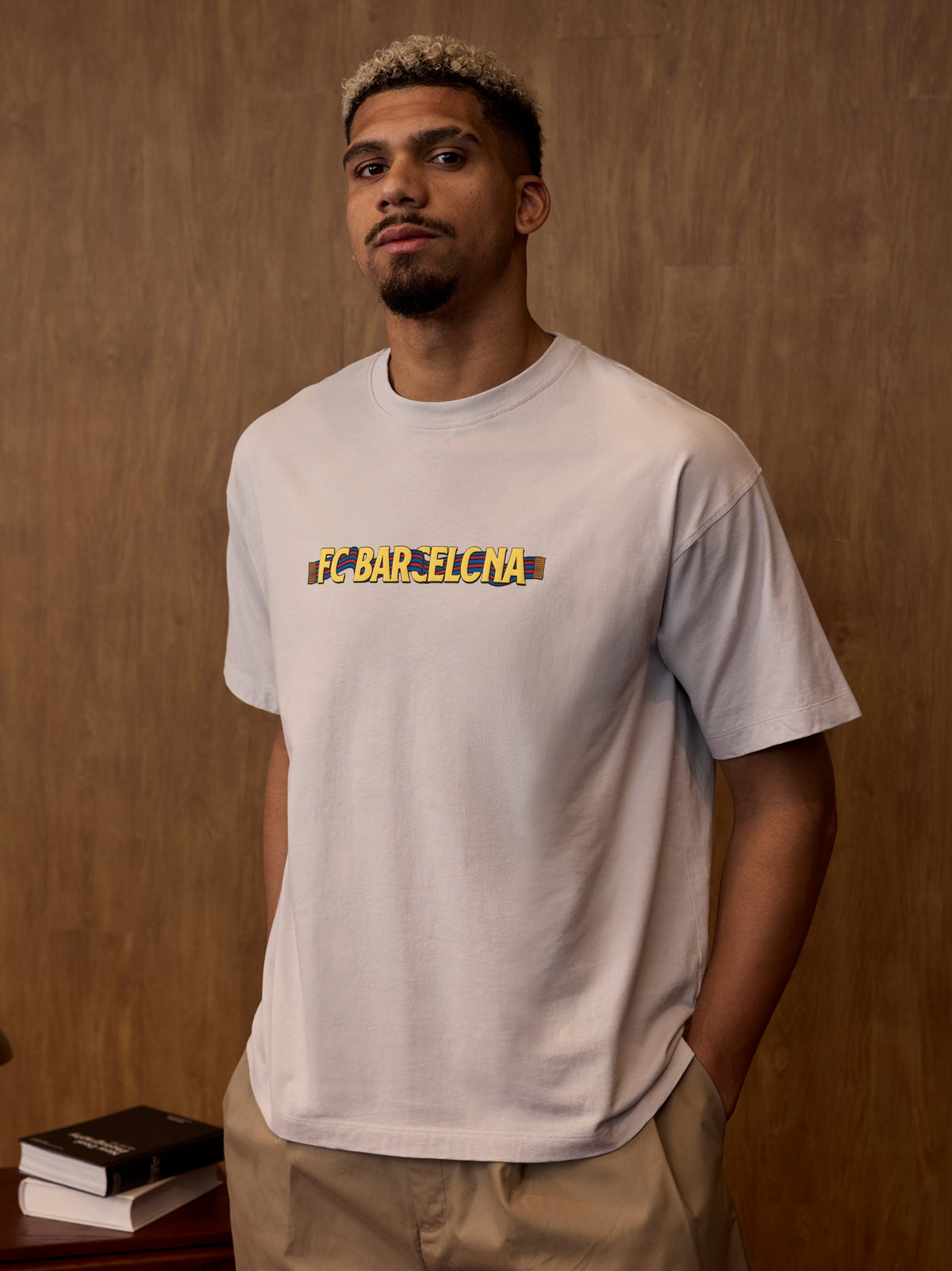 Man wearing a gray t-shirt with 'FC Barcelona' printed on it against a wooden background.