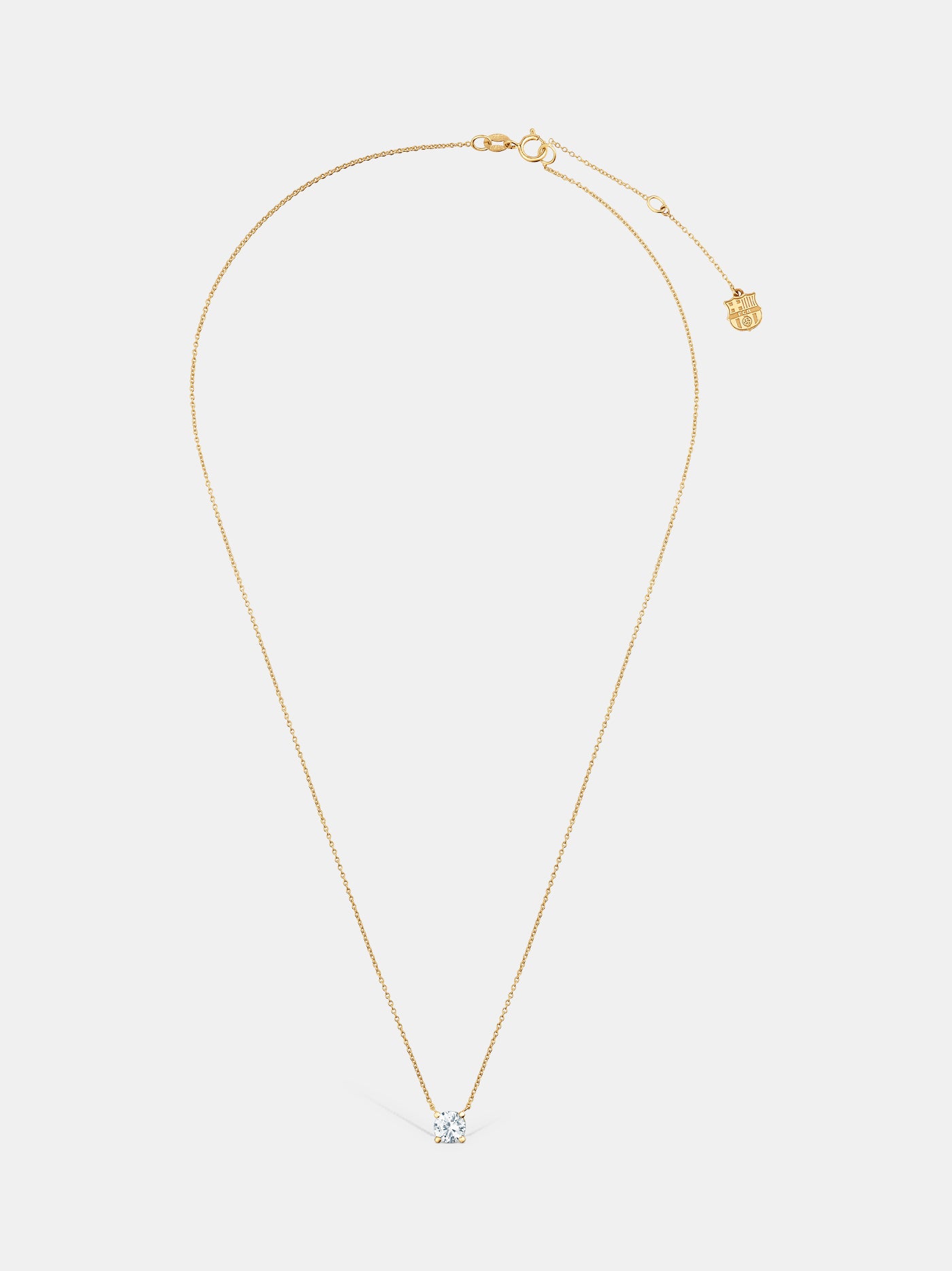 Elegant gold necklace featuring a central diamond-like stone and a small hanging FC Barcelona crest charm near the clasp.


