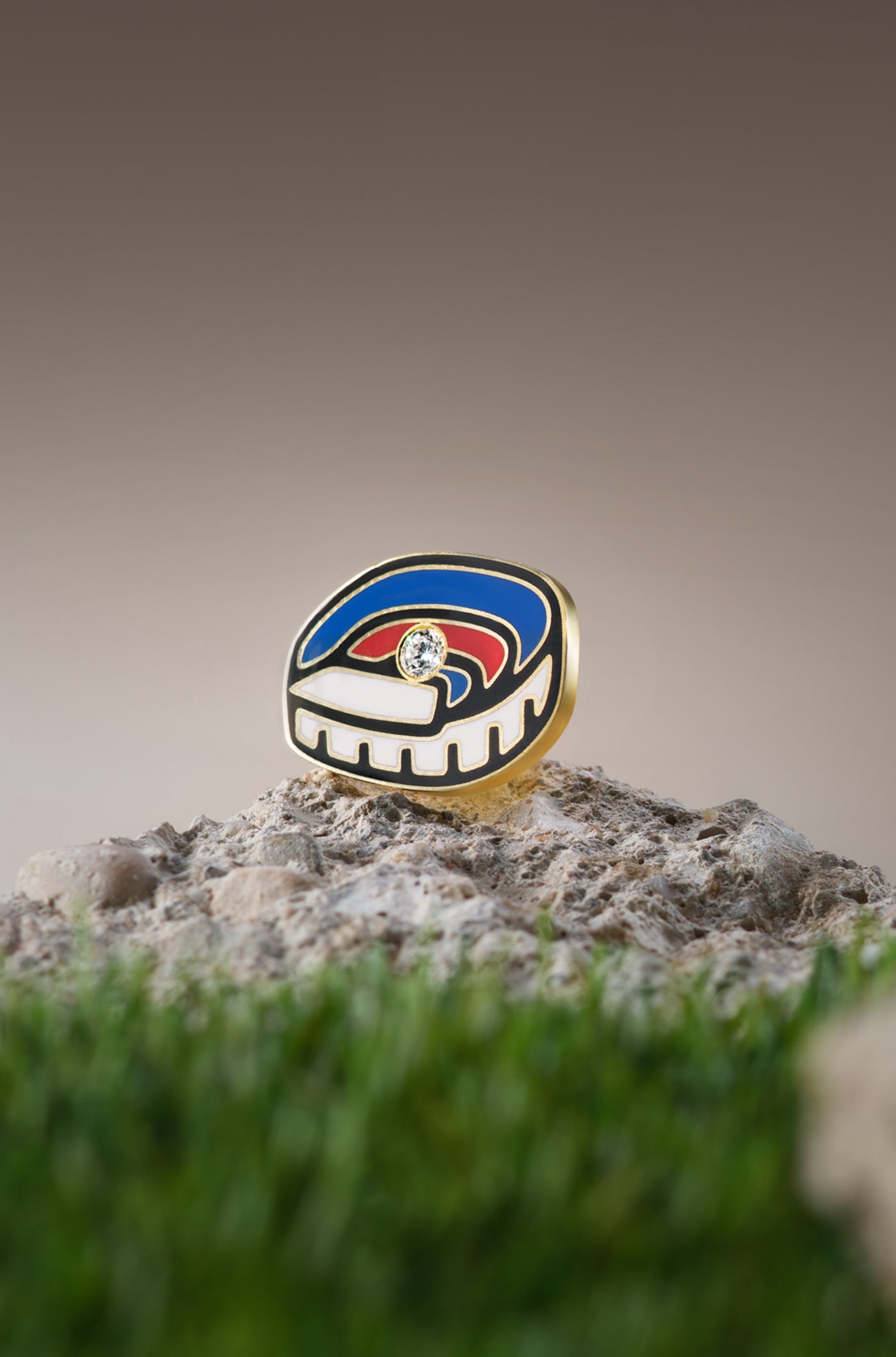 Gold pin featuring an abstract design of the Olympic Stadium in red, blue, and white enamel, with a diamond at the center.