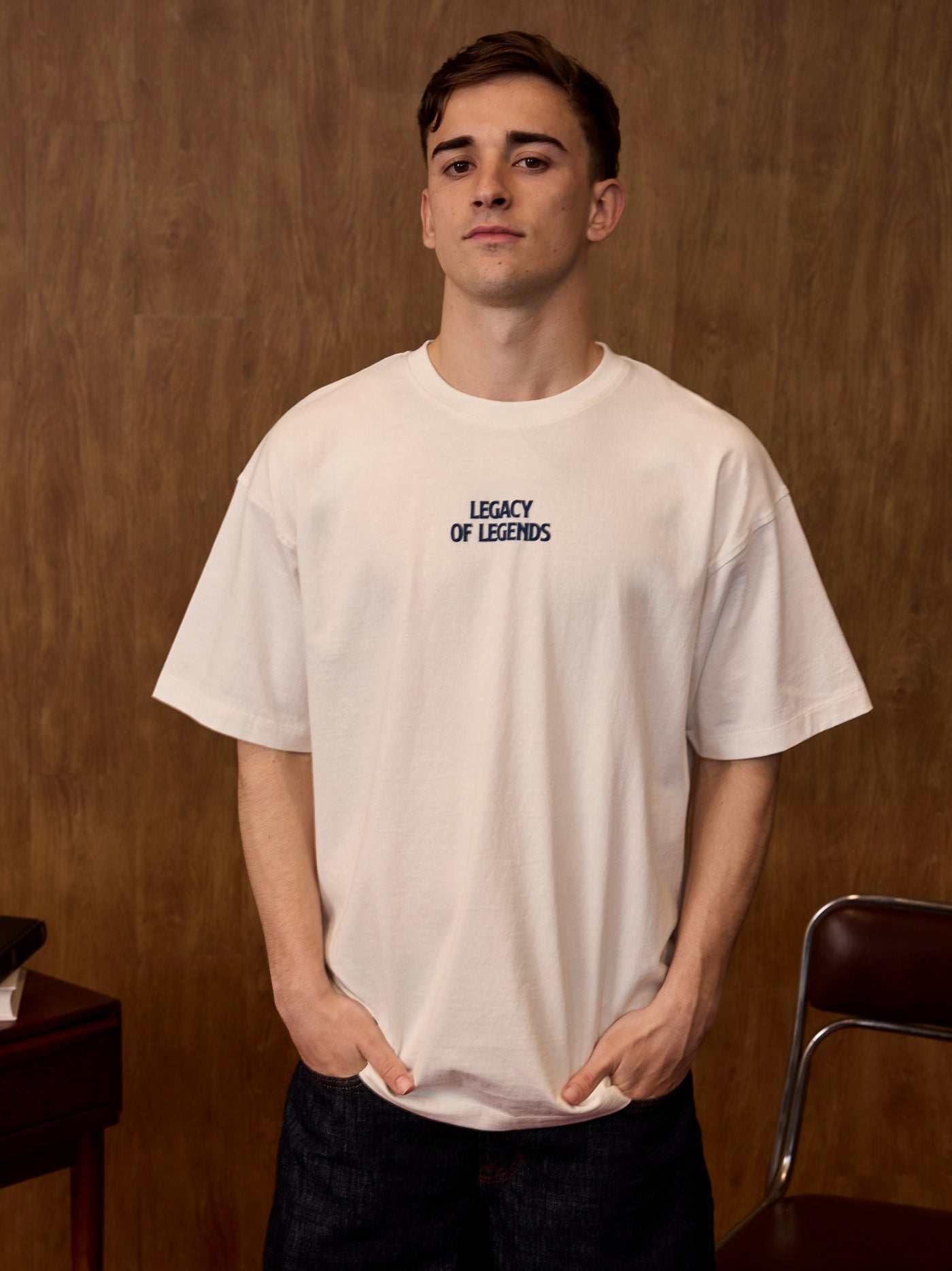 Person wearing a white t-shirt with 'Legacy of Legends' text in a room with wooden walls.