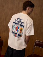 Person wearing a white t-shirt with 'Legacy of Legends' design on the back, standing against a wooden wall.