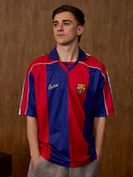 Vista frontal d'un model amb una samarreta del FC Barcelona amb ratlles verticals vermelles i blaves, coll blau i l'escut del Barça al pit.