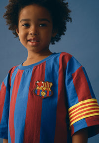 Child wearing a red and blue striped shirt with a logo on a blue background