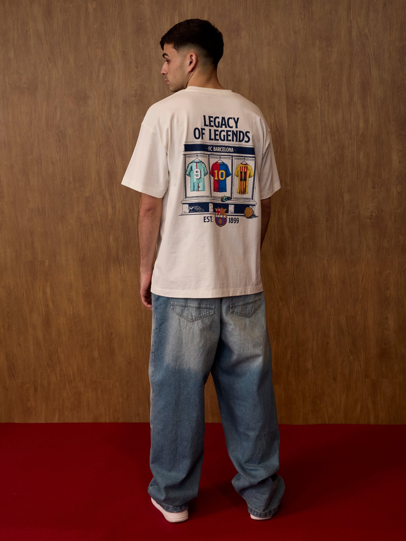 Person wearing a t-shirt with 'Legacy of Legends' design on the back, standing against a wooden wall.