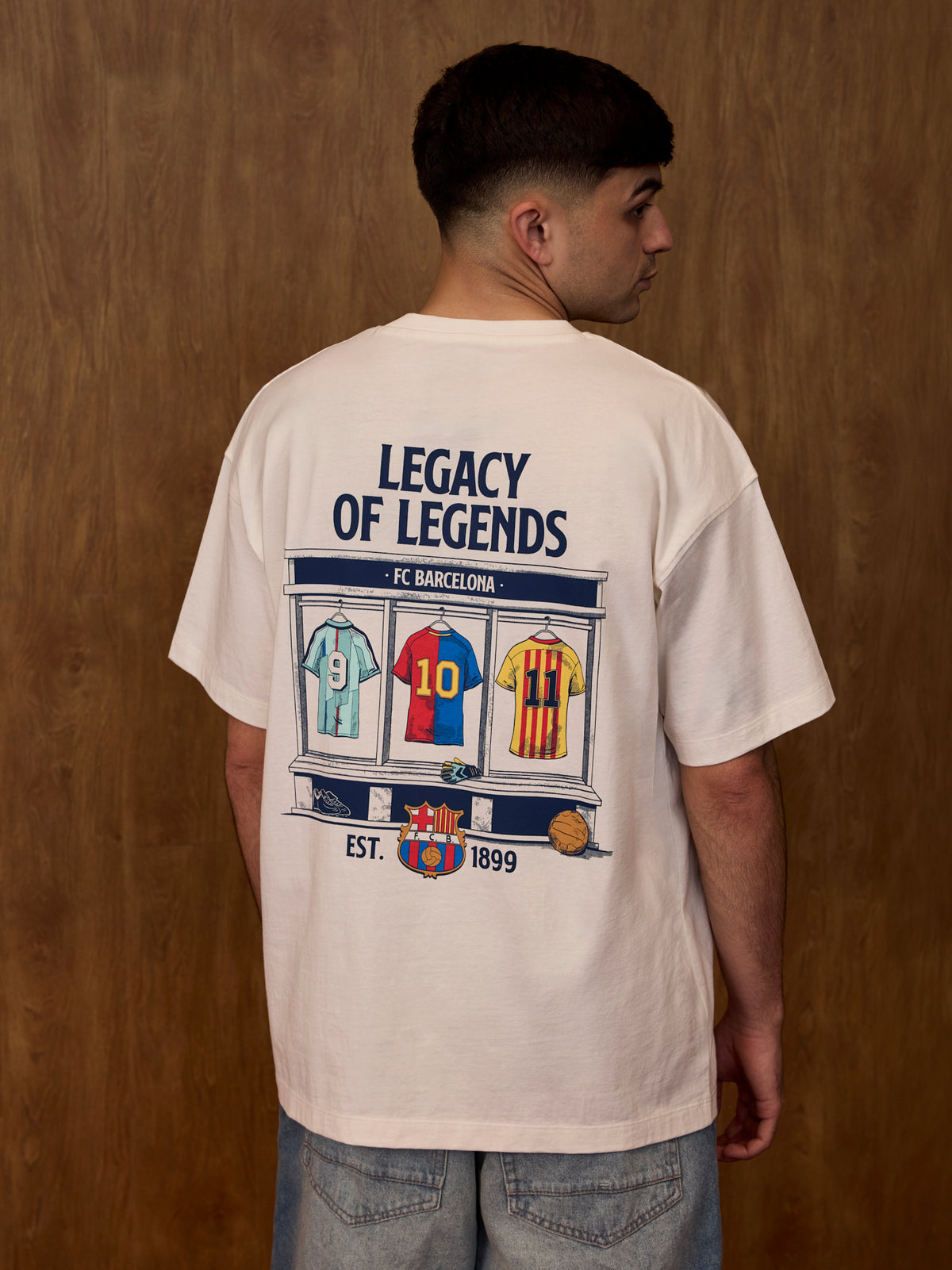 Person wearing a t-shirt with 'Legacy of Legends' and FC Barcelona design on the back against a wooden wall.