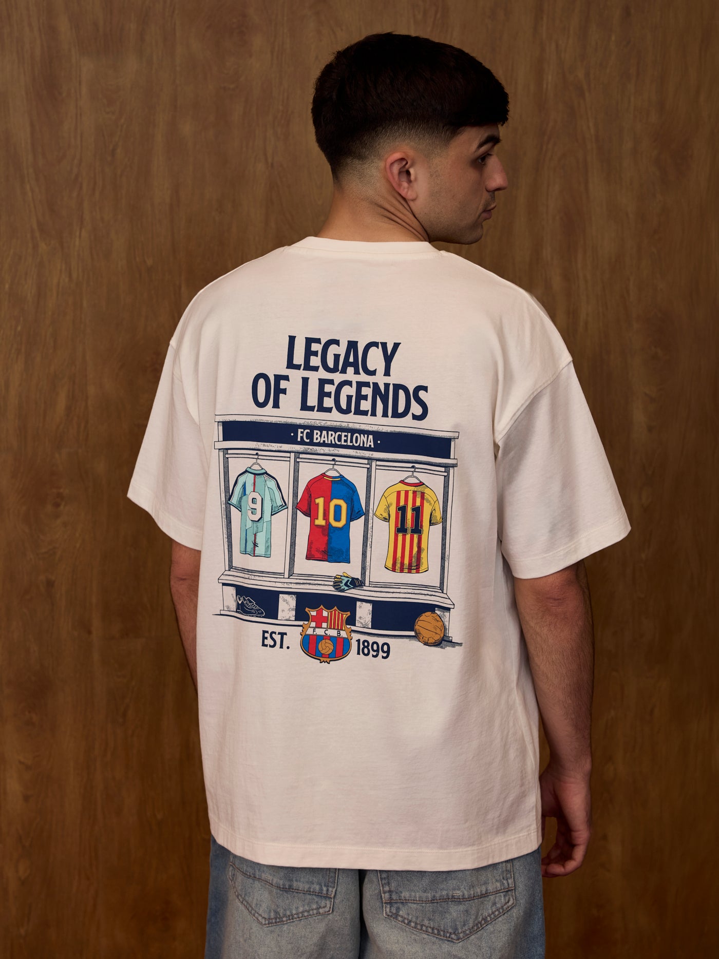 Person wearing a t-shirt with 'Legacy of Legends' and FC Barcelona design on the back against a wooden wall.